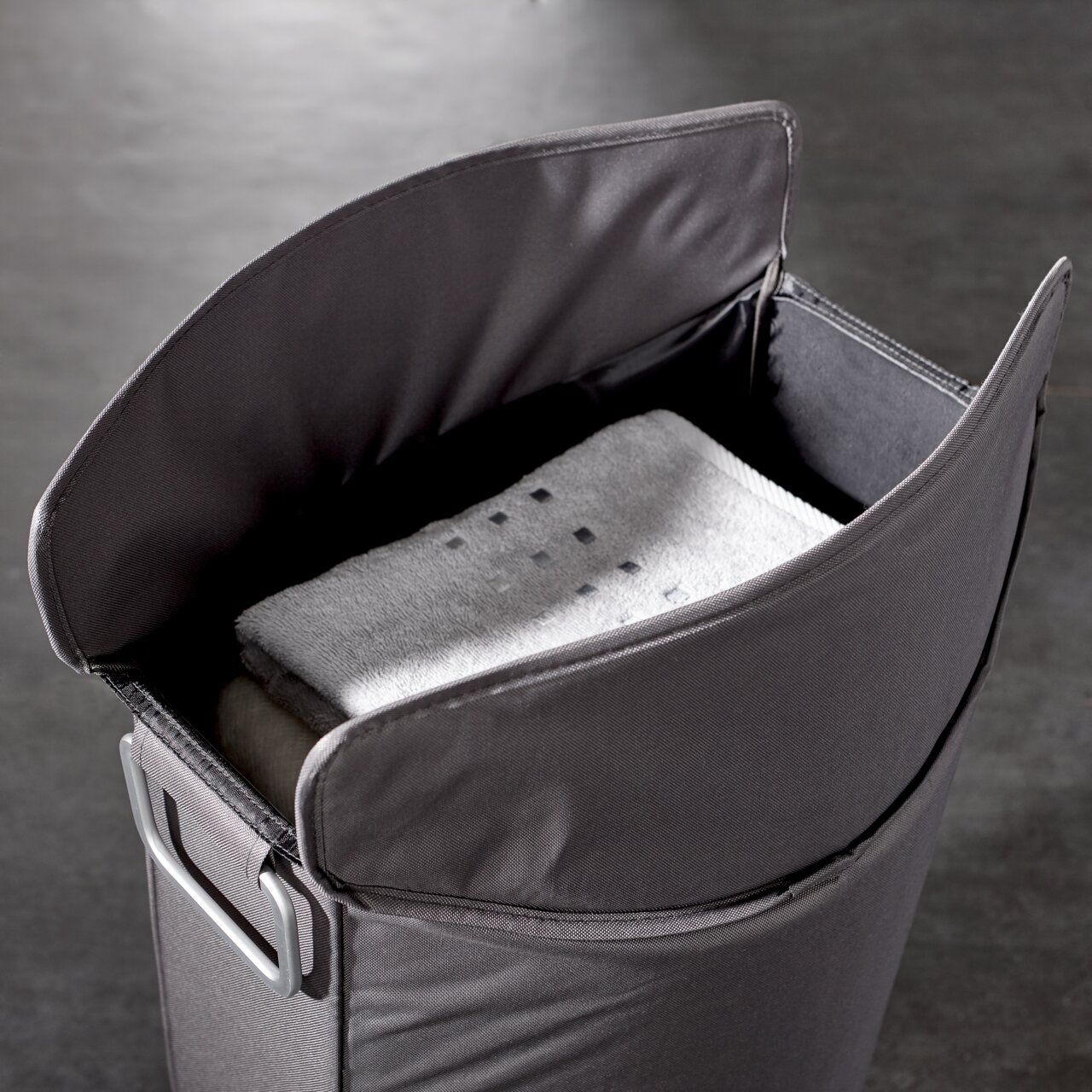 Grauer Wäschesammler mit geöffnetem Deckel, gefüllt mit Handtüchern, aus der Vogelperspektive.