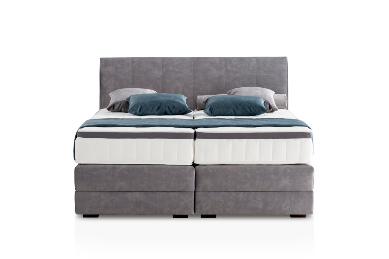 Frontale Ansicht eines grauen Boxspringbetts mit zwei Kissen und einer Decke in Blau- und Grautönen.