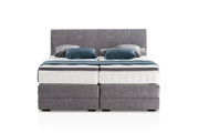 Frontale Ansicht eines grauen Boxspringbetts mit zwei Kissen und einer Decke in Blau- und Grautönen.