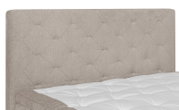 Nahaufnahme eines Boxspringbetts mit gepolstertem Kopfteil in beige, seitliche Perspektive