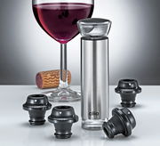 Weinpumpe CAMPANIA aus Edelstahl mit vier schwarzen Vakuumverschlüssen, im Vordergrund auf einem Tisch, im Hintergrund ein gefülltes Weinglas und ein Korken.