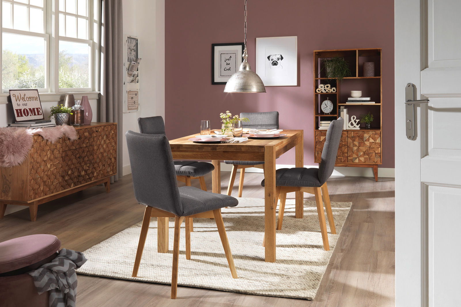 Esszimmer mit einem Holztisch und vier grauen Stühlen, umgeben von stilvoller Dekoration. Perspektive von der Tür aus.