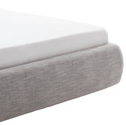 Nahaufnahme eines grauen Polsterbetts mit weißer Matratze, seitliche Perspektive.