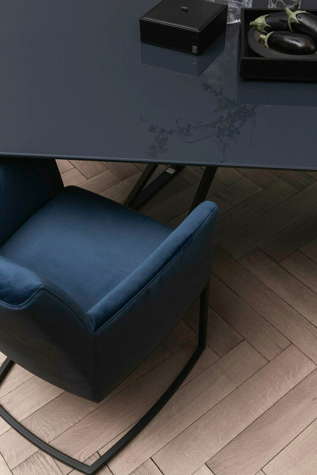 Freischwinger-Sessel in dunkelblauem Stoff, von oben betrachtet, neben einem eleganten Tisch auf einem Holzboden.