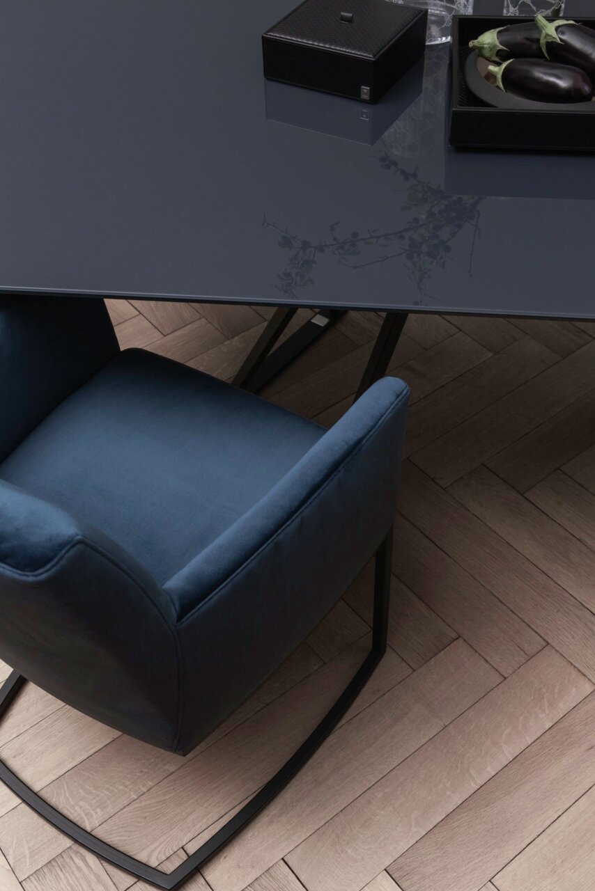 Een zweefstoel in donkerblauwe stof, gezien van bovenaf, naast een elegante tafel op een houten vloer.