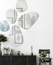 Facettenspiegel in organischen Formen an einer weißen Wand, umgeben von Pflanzen und Wandkunst, aus der Frontalperspektive betrachtet.