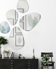 Facettenspiegel in organischen Formen an einer weißen Wand, umgeben von Pflanzen und Wandkunst, aus der Frontalperspektive betrachtet.