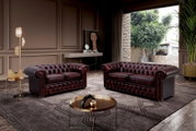 Twee elegante, donkerrode Chesterfield-banken in een stijlvol ingerichte woonkamer met uitzicht op een tuin door een groot raam.
