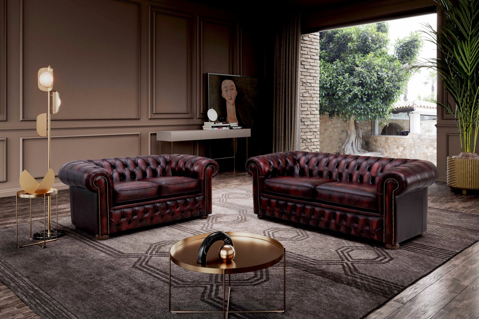 Twee elegante, donkerrode Chesterfield-banken in een stijlvol ingerichte woonkamer met uitzicht op een tuin door een groot raam.