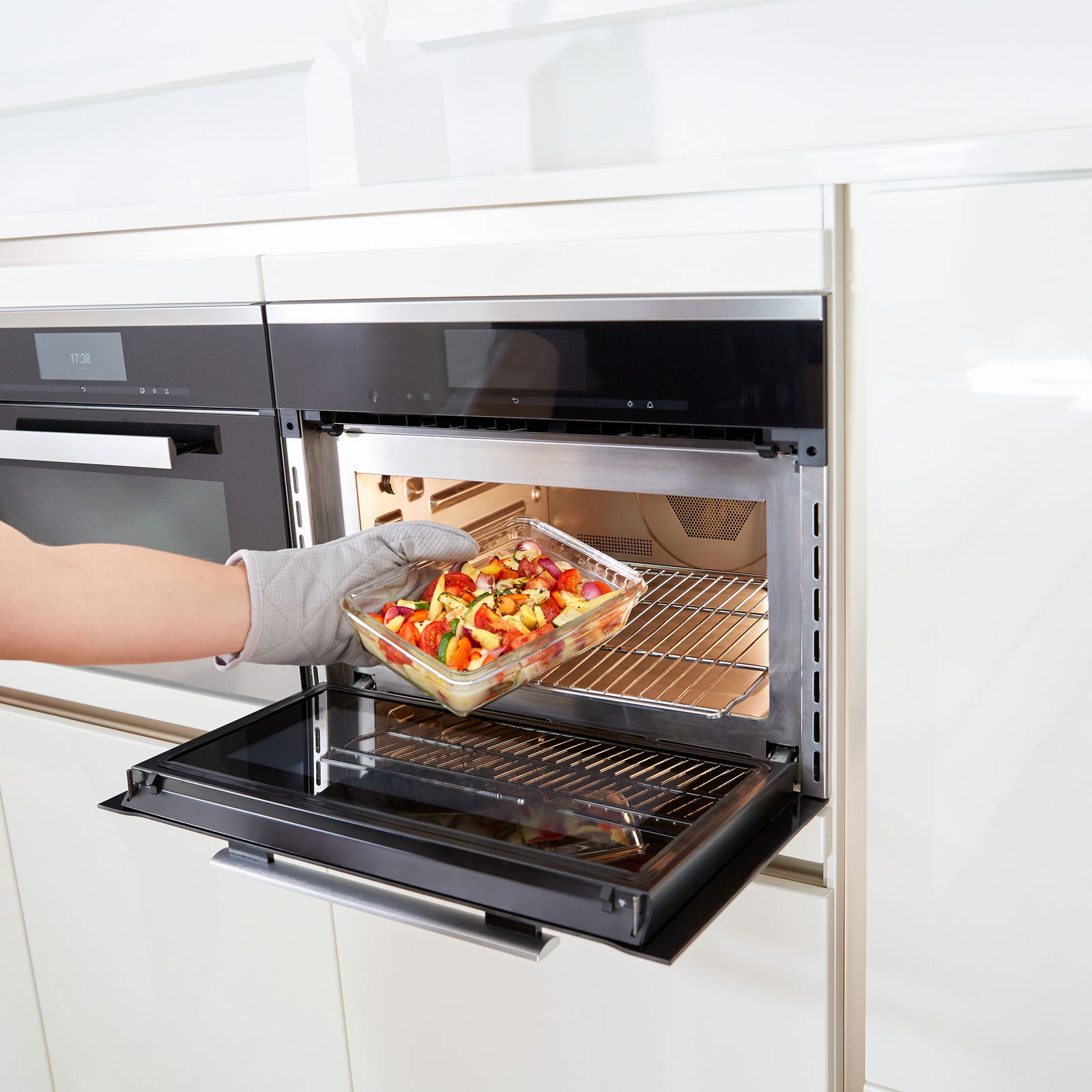 Rechteckige Glasform mit 3,00L Fassungsvermögen, gefüllt mit Gemüse, wird aus einem modernen Backofen entnommen. Perspektive von der Seite.