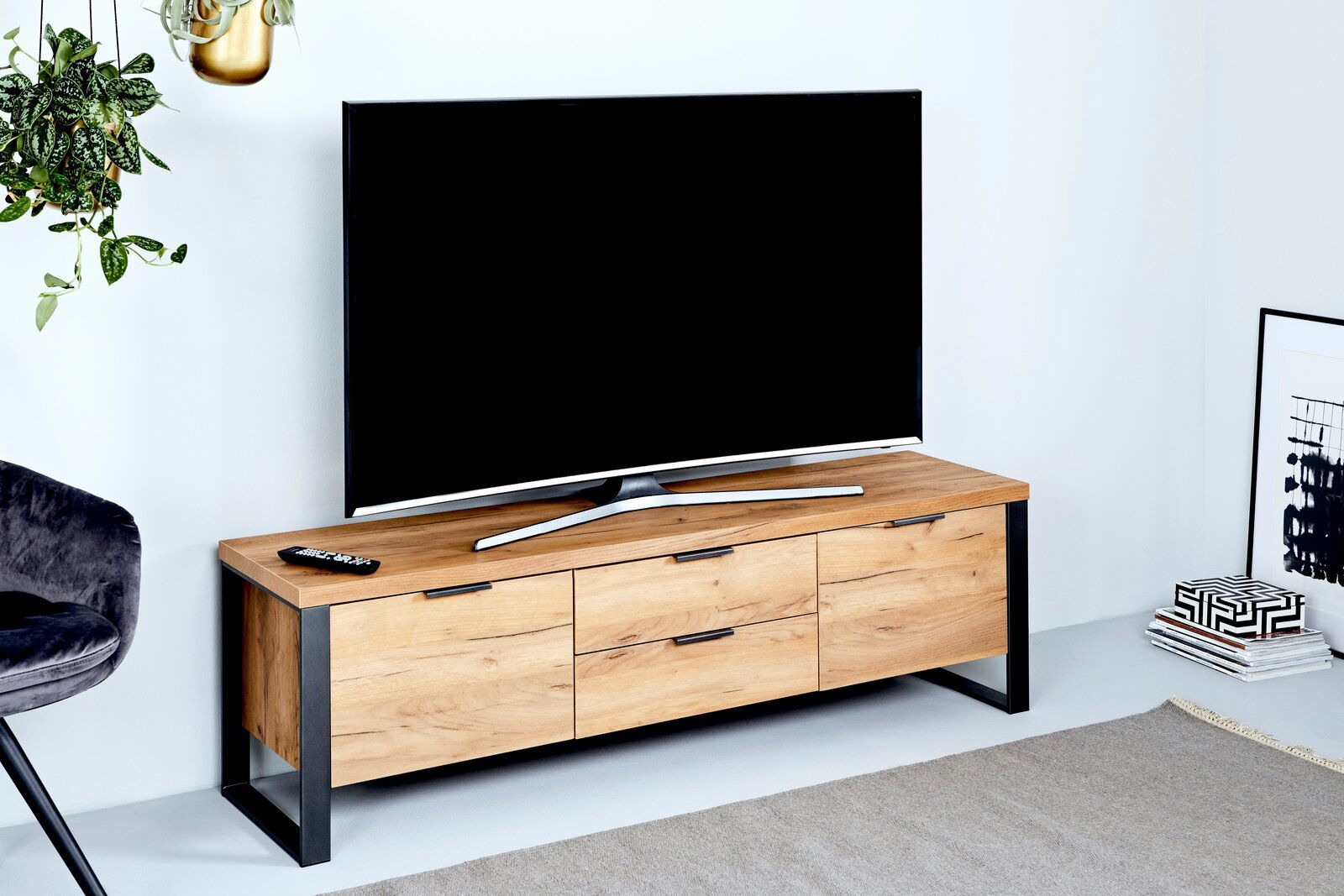 TV-Lowboard aus Holz mit Metallrahmen, frontal fotografiert, mit einem Fernseher darauf und dekorativen Elementen daneben.
