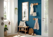 Eingangsbereich mit einer Garderobenbank aus Holz, einem Spiegel und Hakenleisten an einer blauen Wand. Perspektive von der Tür aus.