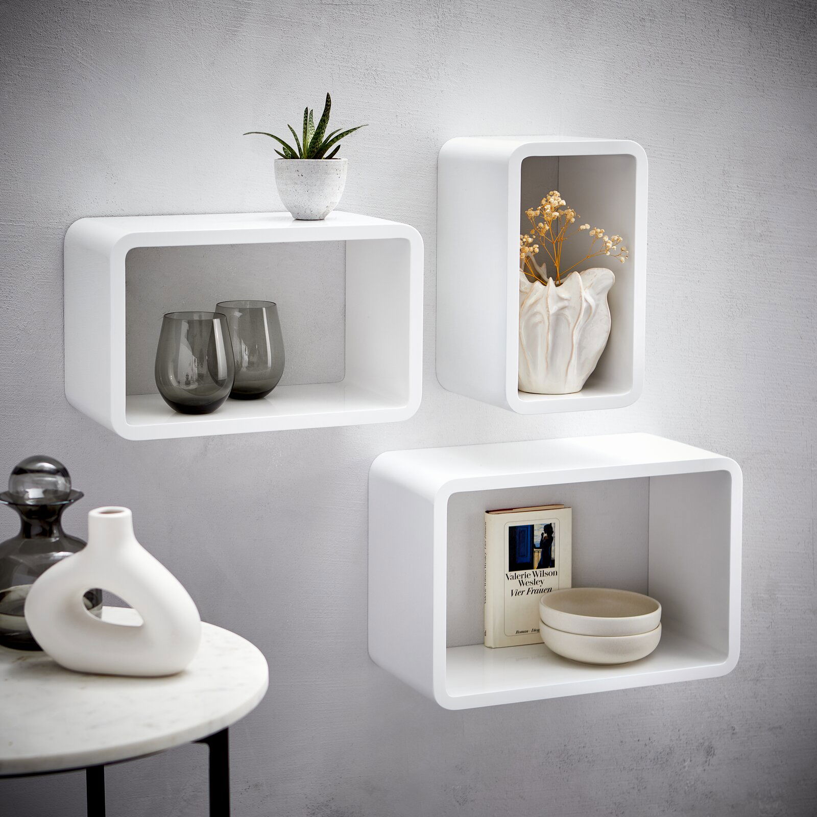 XORA Wandregal-3er-Set CURVE Wandregal-3er-Set in Weiß, bestehend aus drei rechteckigen Regalen, dekoriert mit Pflanzen, Vasen und Büchern, an einer grauen Wand montiert, seitliche Perspektive.