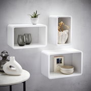 Wandregal-3er-Set in Weiß, bestehend aus drei rechteckigen Regalen, dekoriert mit Pflanzen, Vasen und Büchern, an einer grauen Wand montiert, seitliche Perspektive.