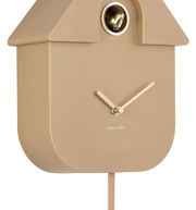 Seitliche Ansicht einer modernen, beige-farbenen Wanduhr in Form eines Vogelhauses mit goldenen Zeigern und einem kleinen goldenen Vogel im oberen Bereich.