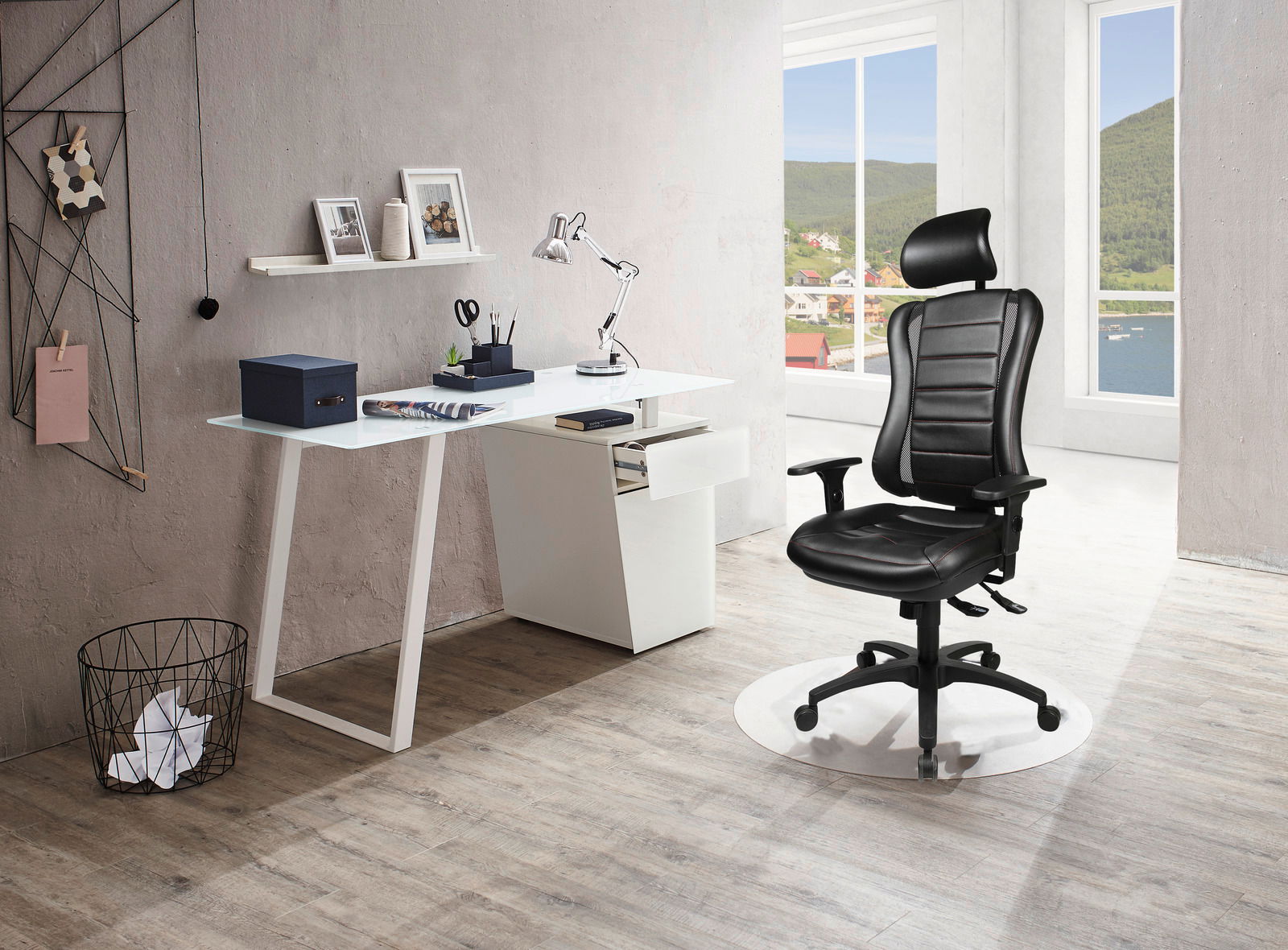 Moderner Schreibtisch mit weißer Tischplatte und Schubladen, daneben ein ergonomischer schwarzer Gaming-Stuhl mit Kopfstütze, seitliche Perspektive.