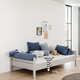 Modernes graues Bett mit blauen und grauen Kissen, seitliche Perspektive, dekoriert mit Wandbildern und Spielzeug.