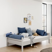 Modernes graues Bett mit blauen und grauen Kissen, seitliche Perspektive, dekoriert mit Wandbildern und Spielzeug.