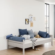 Modernes graues Bett mit blauen und grauen Kissen, seitliche Perspektive, dekoriert mit Wandbildern und Spielzeug.