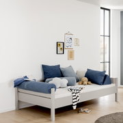 Modernes graues Bett mit blauen und grauen Kissen, seitliche Perspektive, dekoriert mit Wandbildern und Spielzeug.