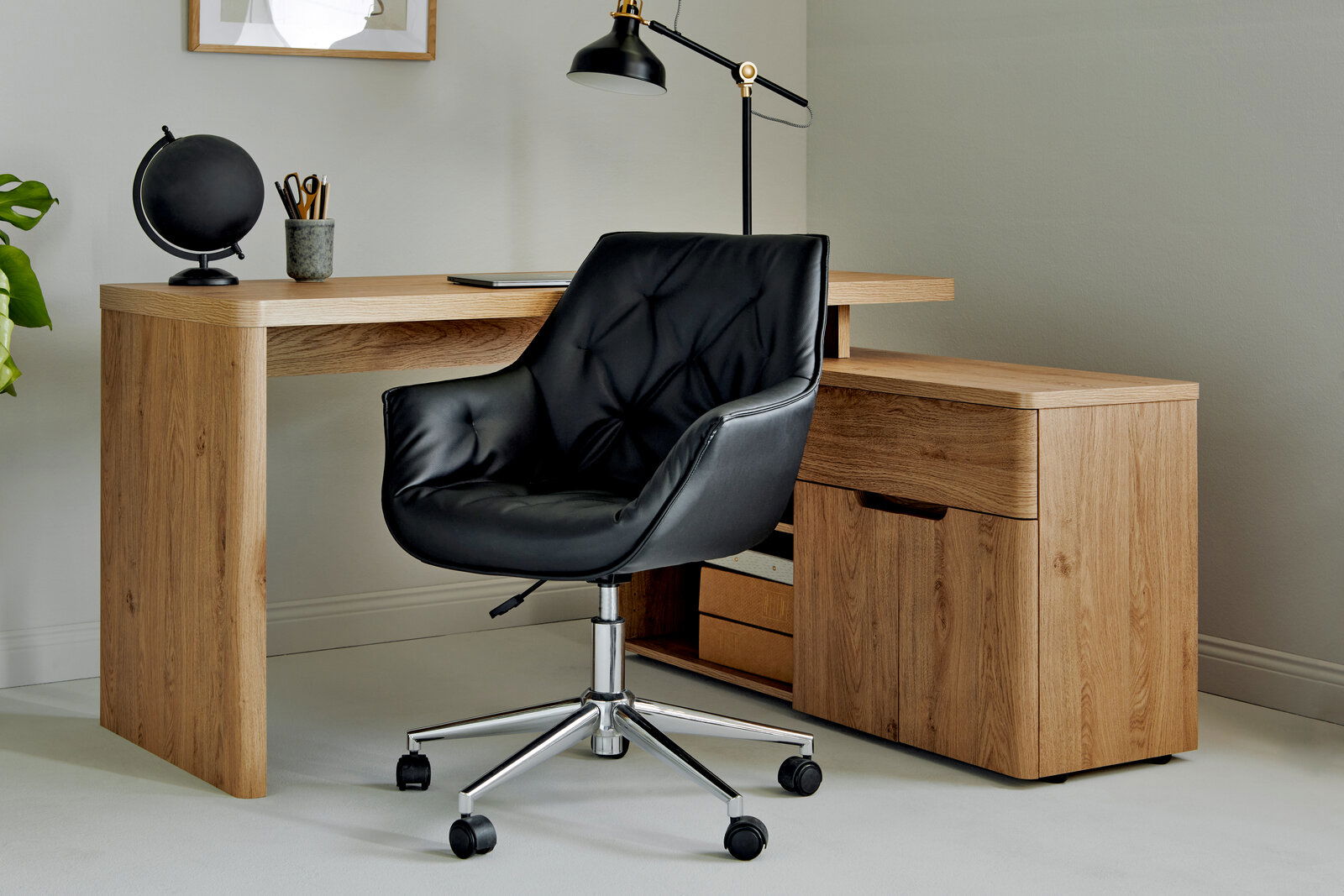 Schwarzer Bürostuhl mit gepolsterter Sitzfläche und Rückenlehne, auf einem verchromten Drehgestell mit Rollen, vor einem Holztisch in einem modernen Büro, seitliche Perspektive.