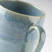 Detailaufnahme einer blau-grau glasierten Keramiktasse mit Henkel, schräg von oben aus seitlicher Perspektive vor hellem Hintergrund