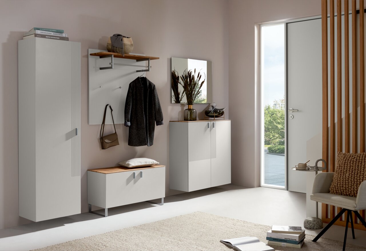 Moderne Garderobeneinrichtung mit Schuhschrank, Garderobenpaneel und Spiegel in einem hellen Raum mit Blick auf eine offene Tür.