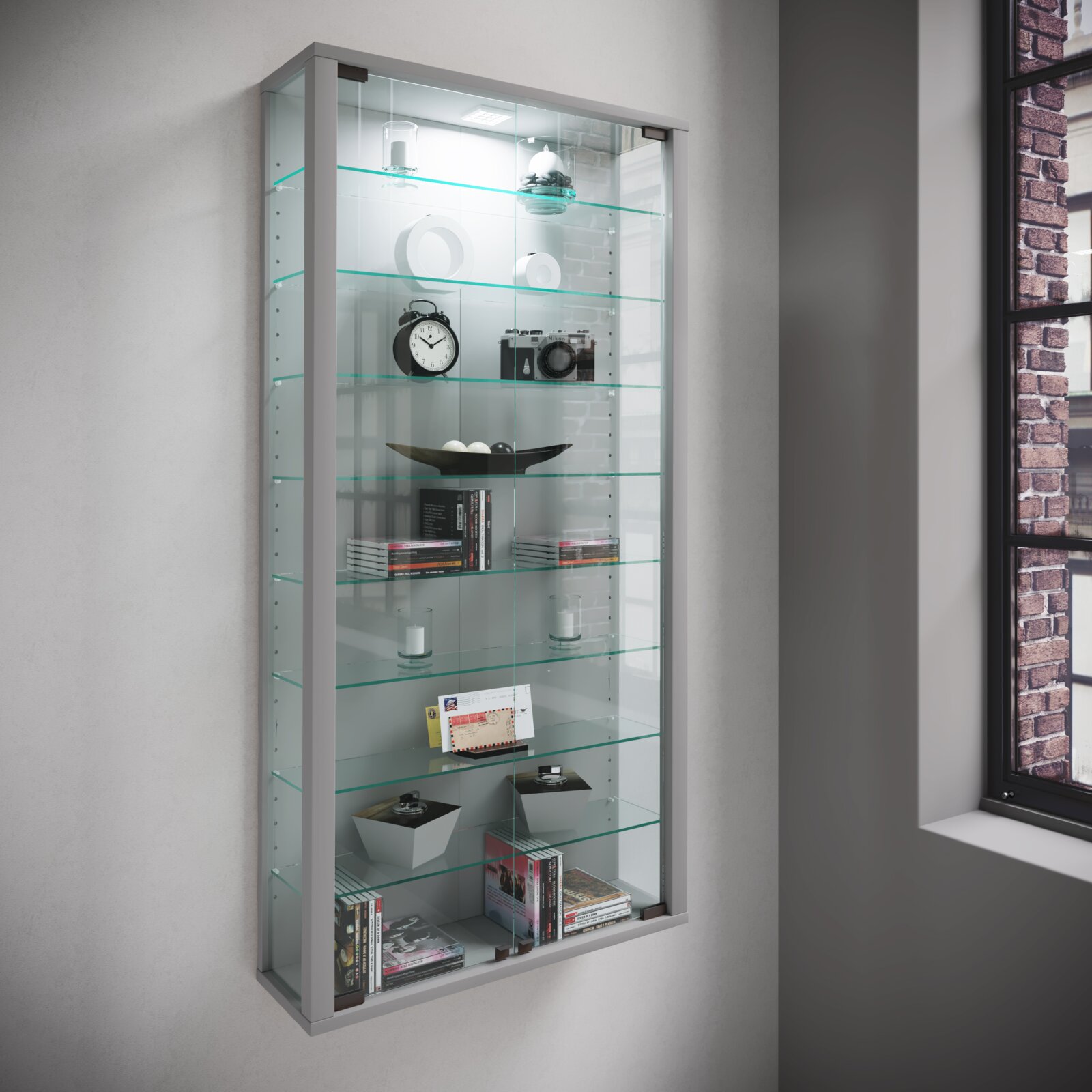 VCM Wandvitrine VITROSA Wandmontierte Glasvitrine mit silbernem Rahmen, Glasböden und LED-Beleuchtung, bestückt mit Deko und Büchern; Ansicht schräg von vorne links.