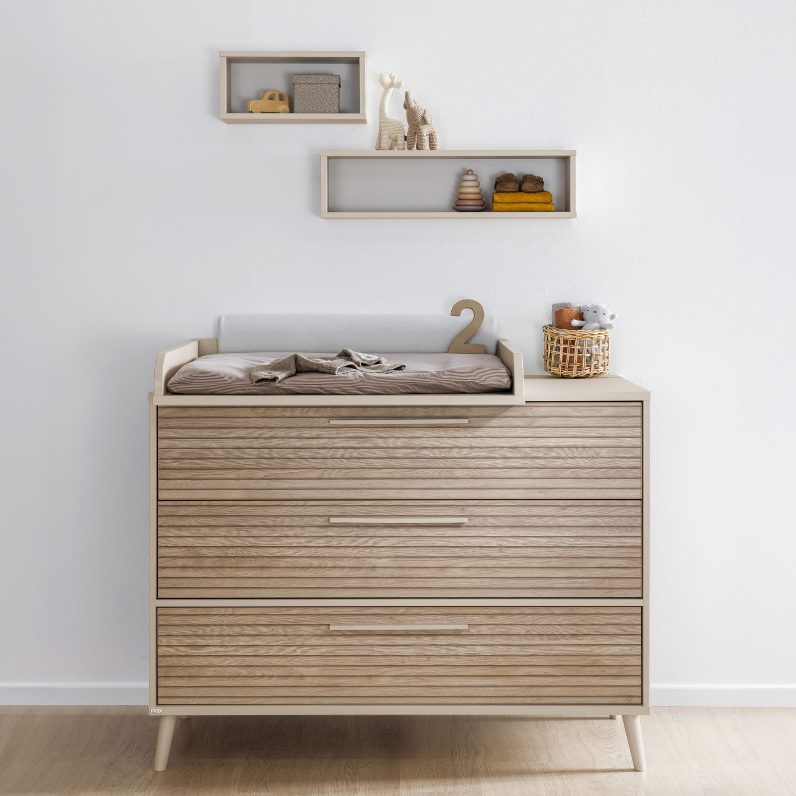 Breite Kommode aus Holz mit drei Schubladen, Wickelauflage und Dekorationen, frontal fotografiert.