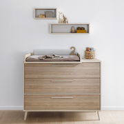 Breite Kommode aus Holz mit drei Schubladen, Wickelauflage und Dekorationen, frontal fotografiert.