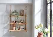 Wandhängeregal aus hellem Holz mit drei Ablagen an Seilen, dekoriert mit Pflanze, Vasen, Uhr und Boxen; seitliche Perspektive im hellen Raum neben Fenster und Tulpenvase.