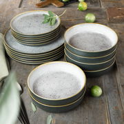 Stapel von grauen Tellern und Schalen mit feinem Muster und goldenen Rändern, auf einem rustikalen Holztisch von oben fotografiert.