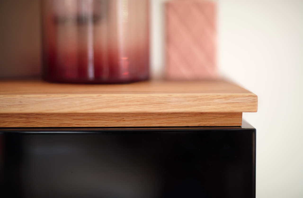 Nahaufnahme eines Möbelstücks mit einer Holzoberfläche und einem schwarzen Element, seitliche Perspektive.