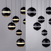 Meerdere zwarte, bolvormige hanglampen met een lichtband rondom hangen aan lange kabels tegen een lichte achtergrond; vooraanzicht vanuit een licht schuin perspectief.