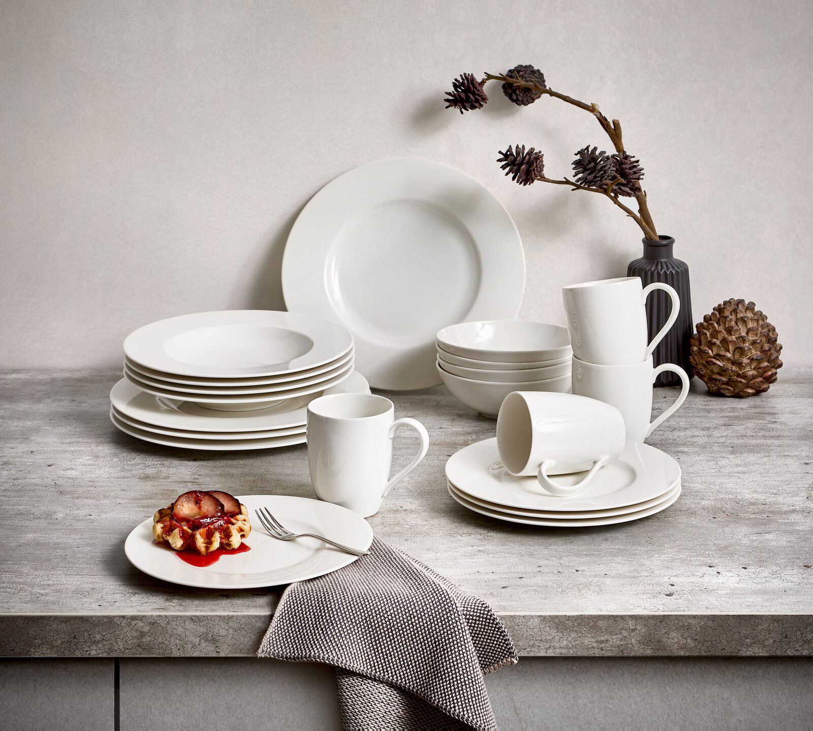 Kombiservice Basic White 20-teilig, bestehend aus Tellern, Tassen und Schalen in schlichtem Weiß, auf einer grauen Tischplatte arrangiert, seitliche Perspektive