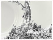Detailaufnahme aus leicht schräger Draufsicht: weißer Porzellanteller mit schwarzem floralen Dekor, Vogelmotiv am Rand und ornamentalem Bordürenmuster.