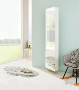 Moderner weißer Drehschuhschrank mit Spiegel, seitliche Perspektive, in einem hellen Raum mit großen Fenstern und stilvoller Dekoration.