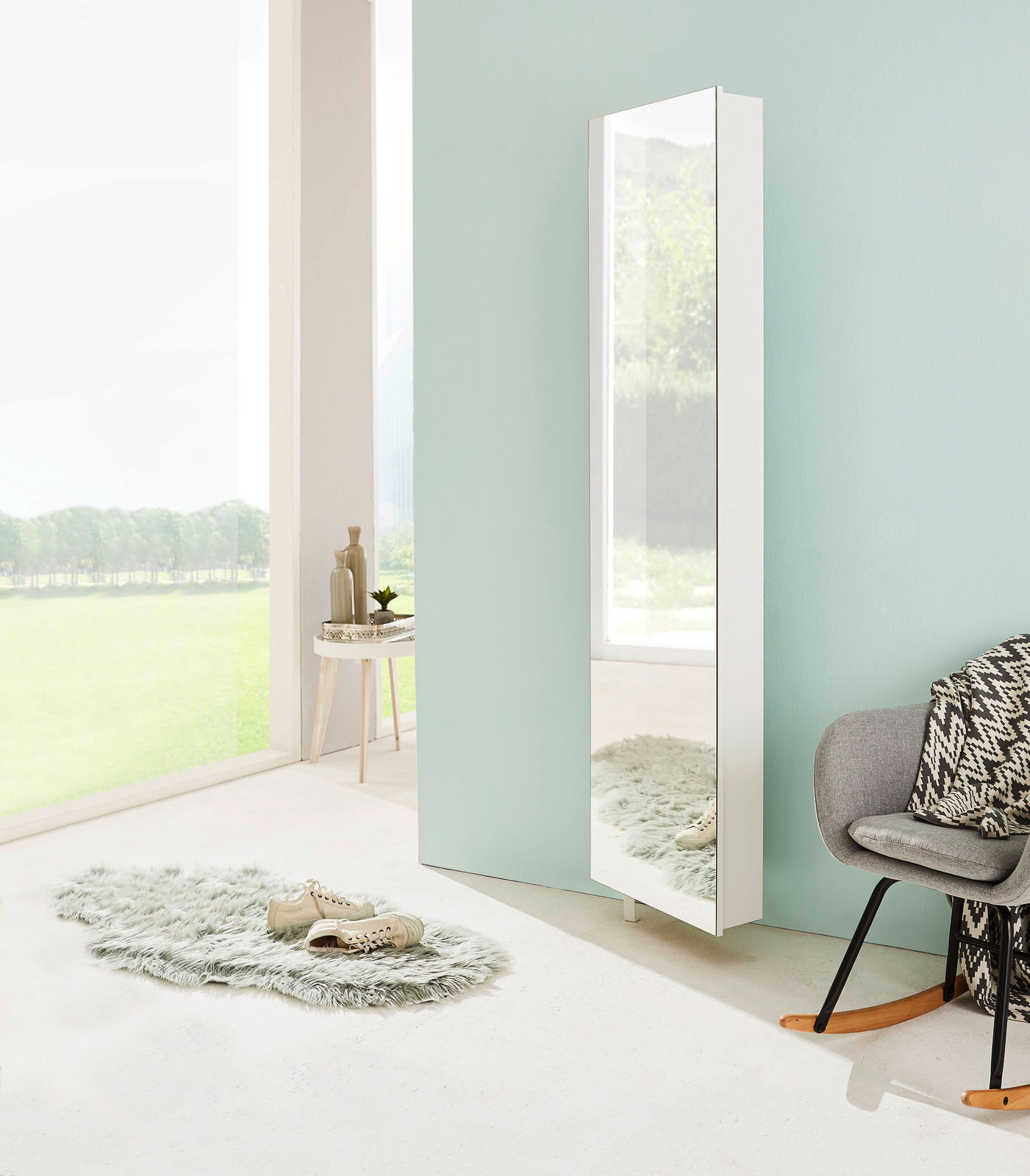 Moderner weißer Drehschuhschrank mit Spiegel, seitliche Perspektive, in einem hellen Raum mit großen Fenstern und stilvoller Dekoration.