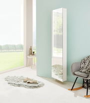 Moderner weißer Drehschuhschrank mit Spiegel, seitliche Perspektive, in einem hellen Raum mit großen Fenstern und stilvoller Dekoration.