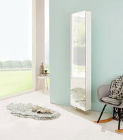 Moderner weißer Drehschuhschrank mit Spiegel, seitliche Perspektive, in einem hellen Raum mit großen Fenstern und stilvoller Dekoration.