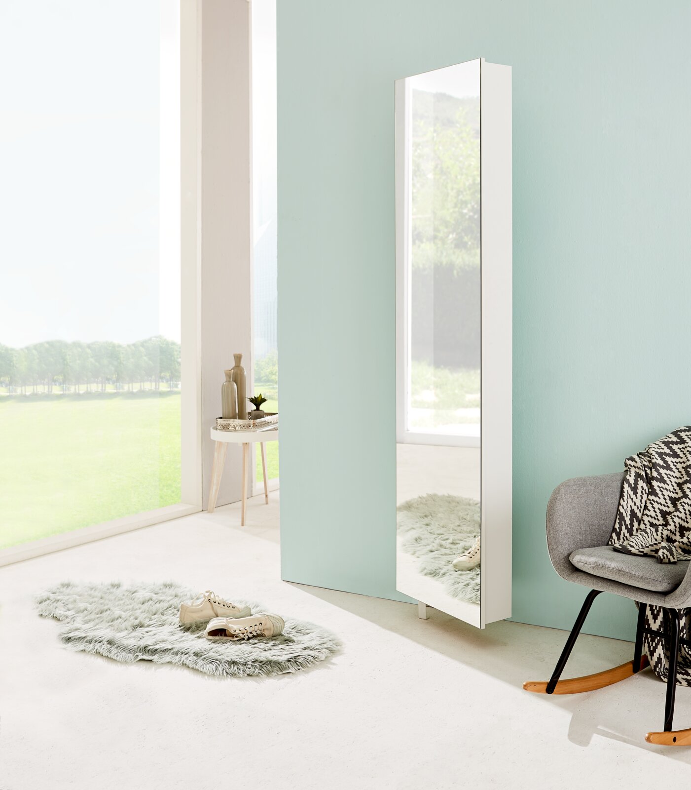 Moderner weißer Drehschuhschrank mit Spiegel, seitliche Perspektive, in einem hellen Raum mit großen Fenstern und stilvoller Dekoration.