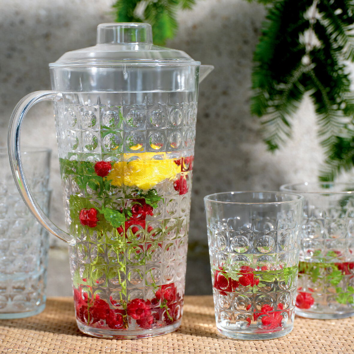 Klares Kannenset mit strukturiertem Design, gefüllt mit Wasser, Zitronenscheiben, roten Beeren und Kräutern, aus seitlicher Perspektive fotografiert.