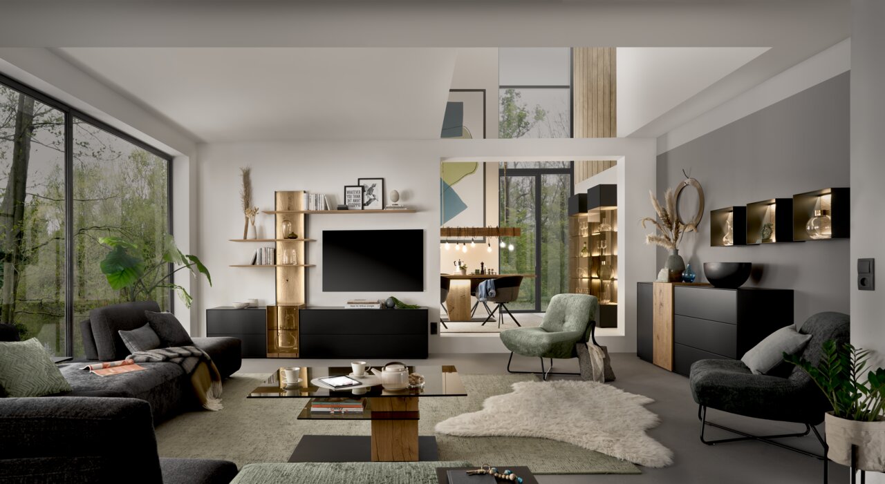 Moderne Wohnzimmeransicht mit eleganter Wandkombination, LED-Beleuchtung und stilvollen Möbeln in einem hellen Raum mit großen Fenstern.