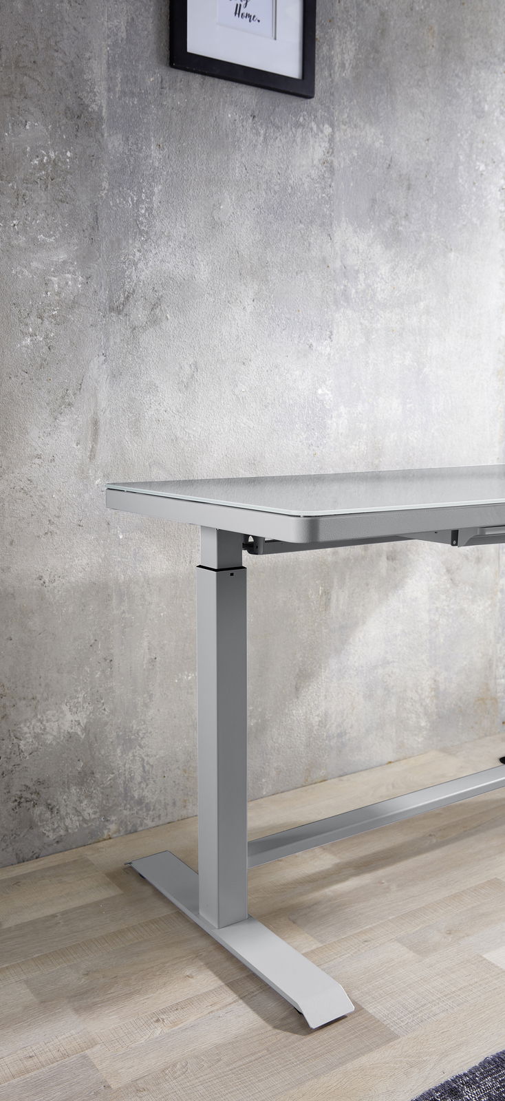 Moderner höhenverstellbarer E-Schreibtisch aus Metall in seitlicher Perspektive, vor einer Betonwand auf Holzboden.