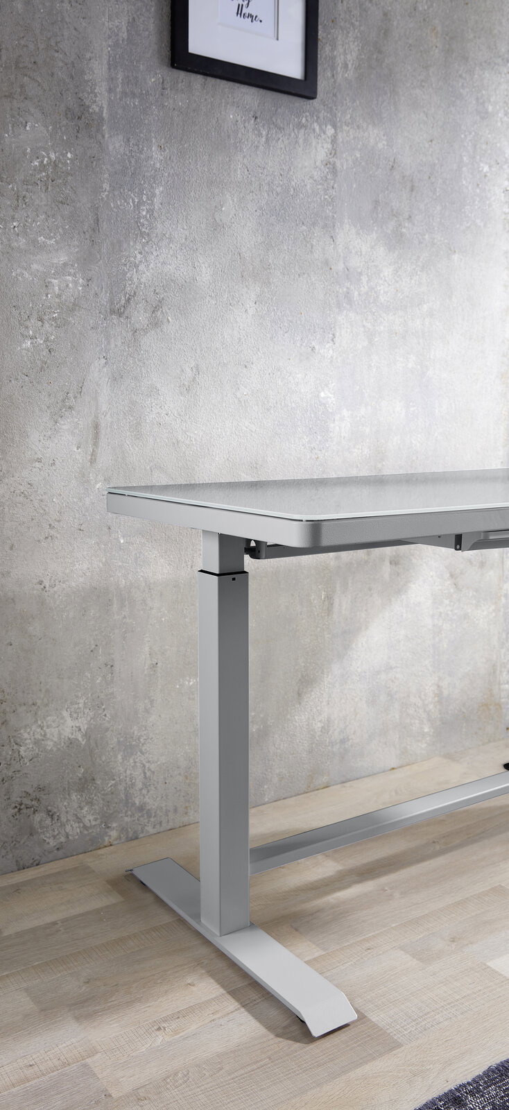 Moderner höhenverstellbarer E-Schreibtisch aus Metall in seitlicher Perspektive, vor einer Betonwand auf Holzboden.
