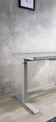 Moderner höhenverstellbarer E-Schreibtisch aus Metall in seitlicher Perspektive, vor einer Betonwand auf Holzboden.