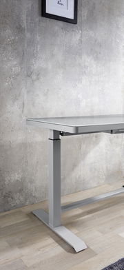 Moderner höhenverstellbarer E-Schreibtisch aus Metall in seitlicher Perspektive, vor einer Betonwand auf Holzboden.