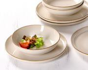 Nahaufnahme eines eleganten, cremefarbenen Speisesets mit Tellern und Schalen, dekoriert mit frischem Salat und Tomaten.