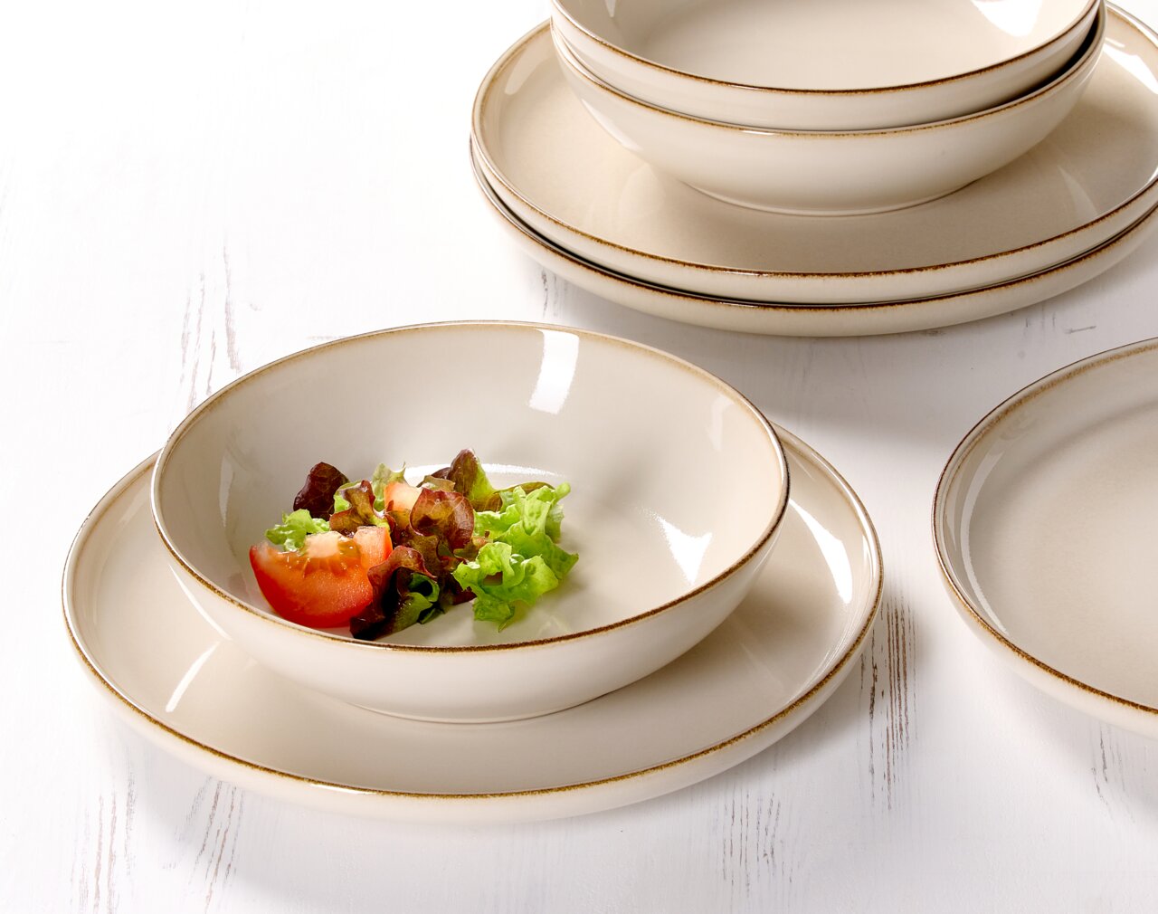 Nahaufnahme eines eleganten, cremefarbenen Speisesets mit Tellern und Schalen, dekoriert mit frischem Salat und Tomaten.