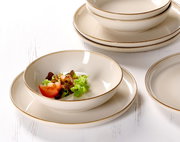 Nahaufnahme eines eleganten, cremefarbenen Speisesets mit Tellern und Schalen, dekoriert mit frischem Salat und Tomaten.